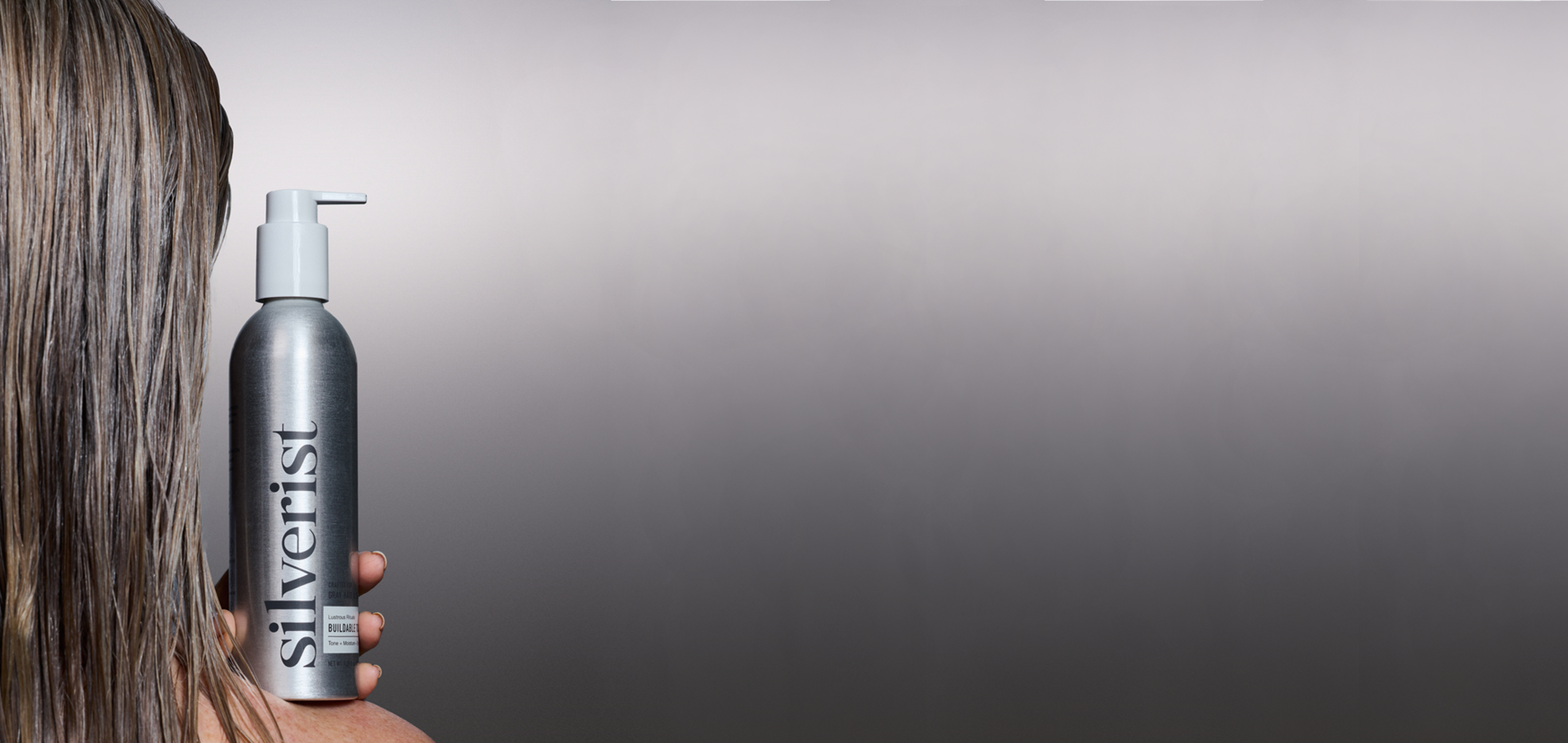 Model with a blonde-gray hair tone holding a Silverist shampoo against a gray background