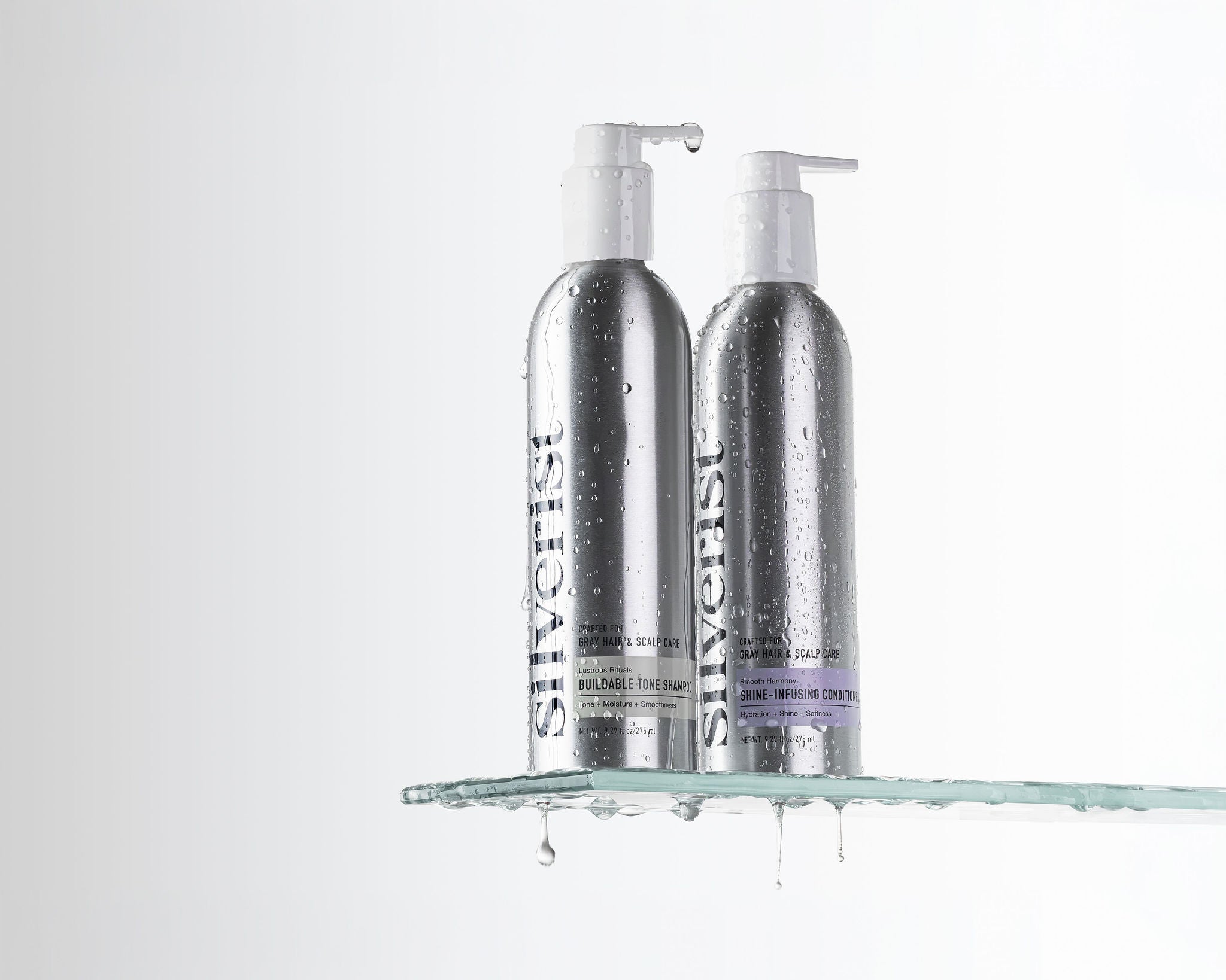 Two silver pump bottles of Silverist haircare products displayed on a clear glass shelf with water droplets against a white background.