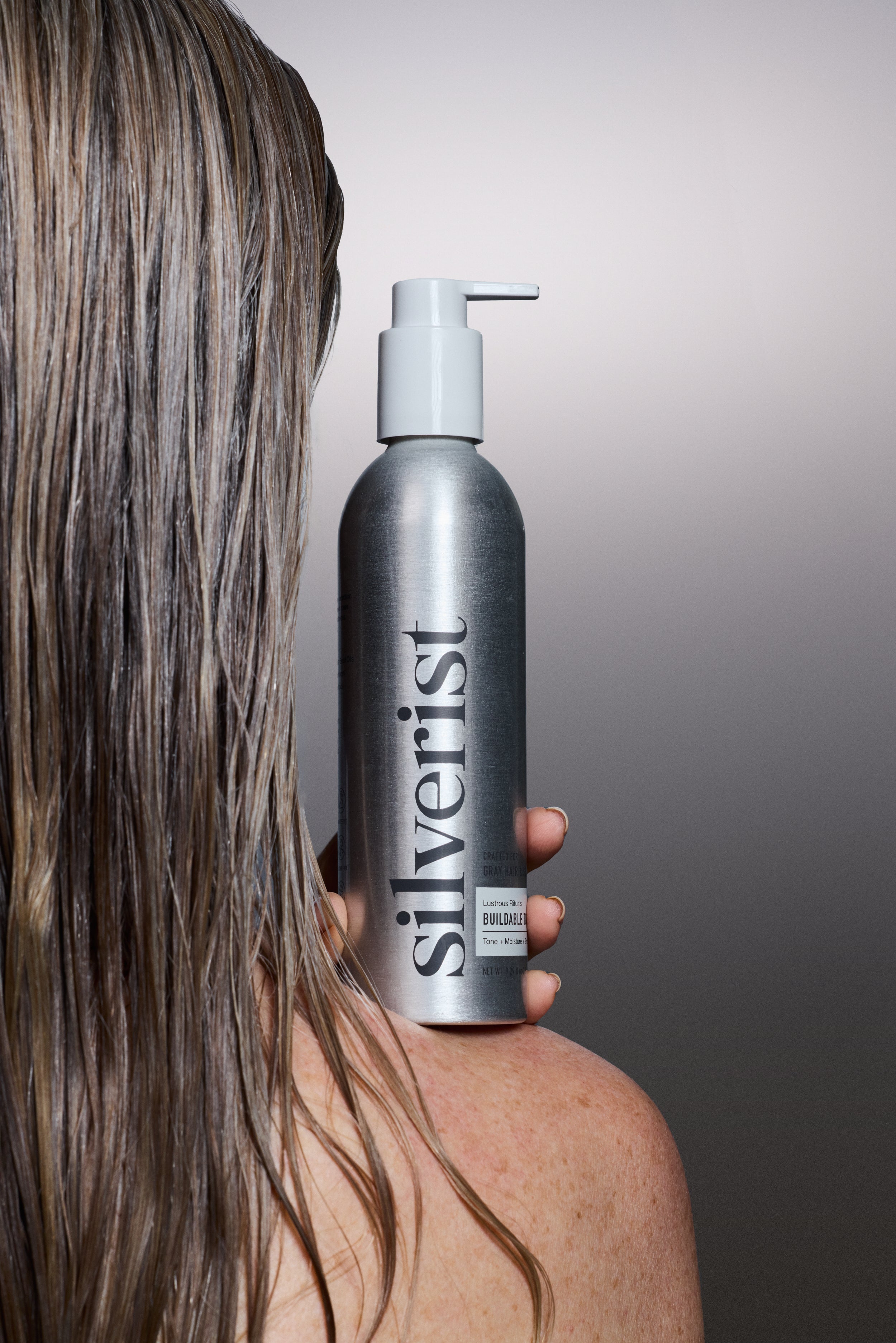 Model with blonde-gray hair tone holding a Silverist shampoo bottle against a gray background